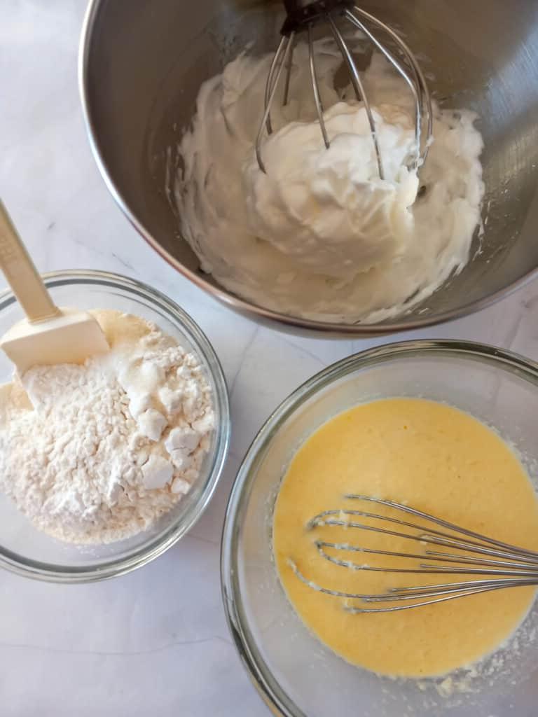 a bowl with beaten egg whites, another bowl with dry ingredients, and a third bowl with wet ingredients.