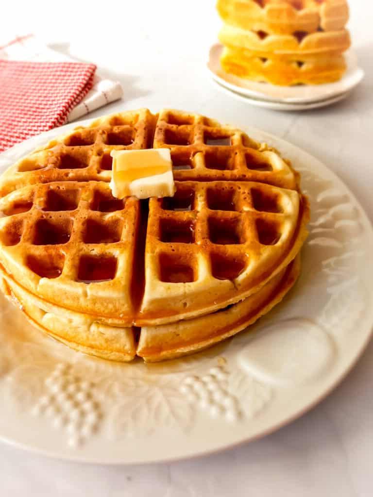 waffles stacked on a plate with butter and syrup on.