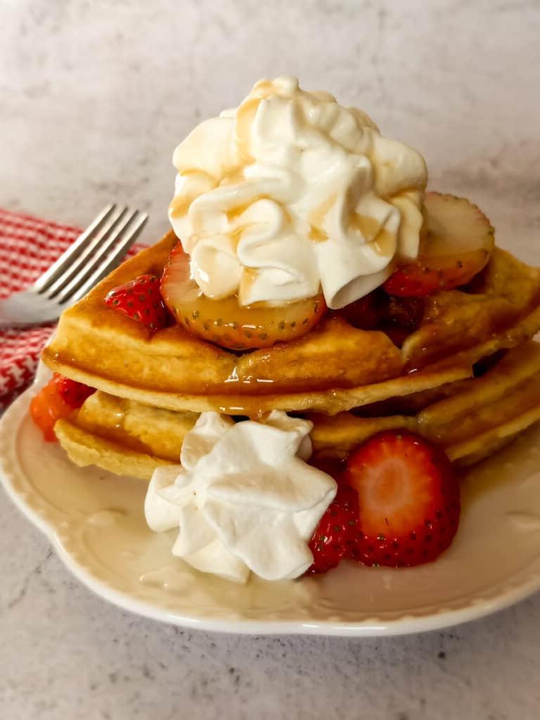waffles topped with strawberries, whipped cream, and syrup.