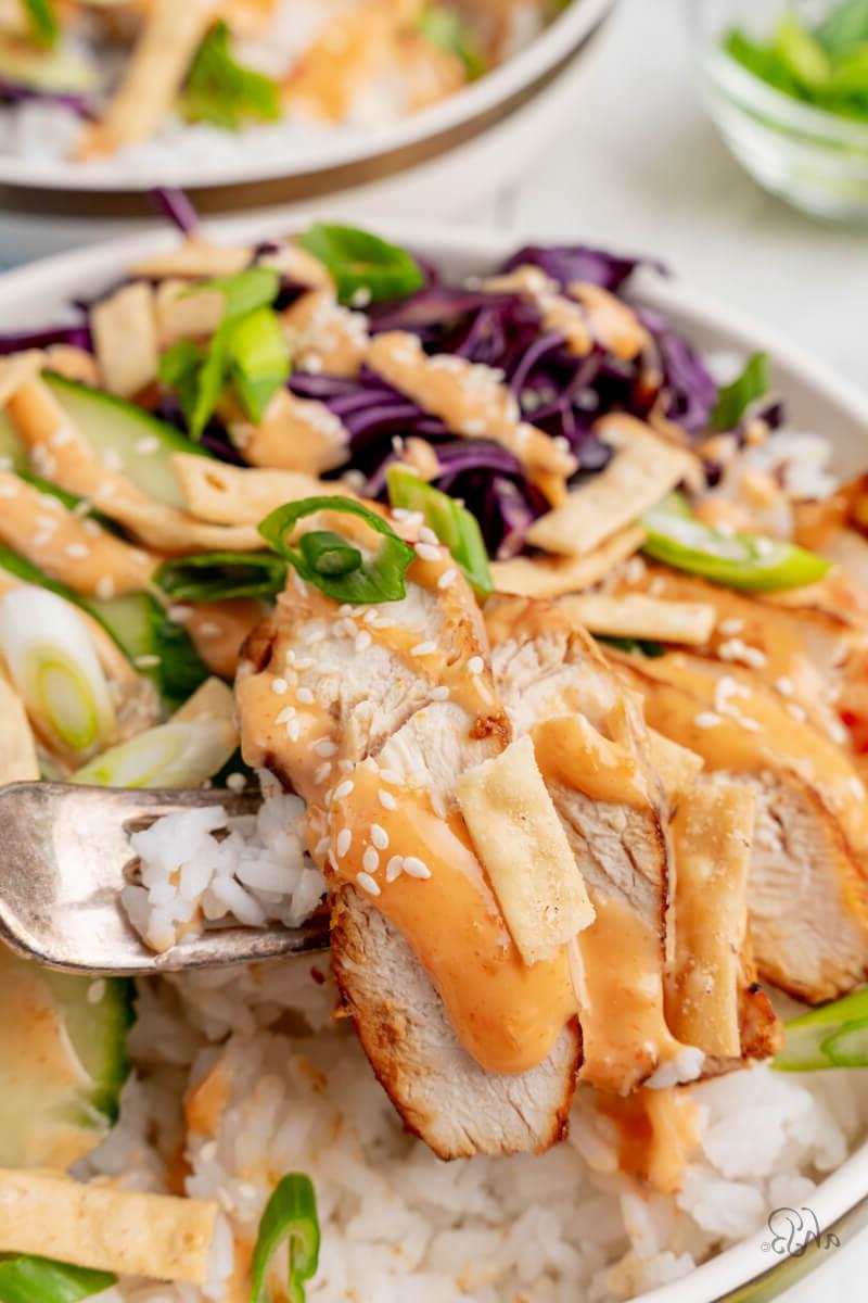 A piece of chicken is taken from the bowl with a fork.