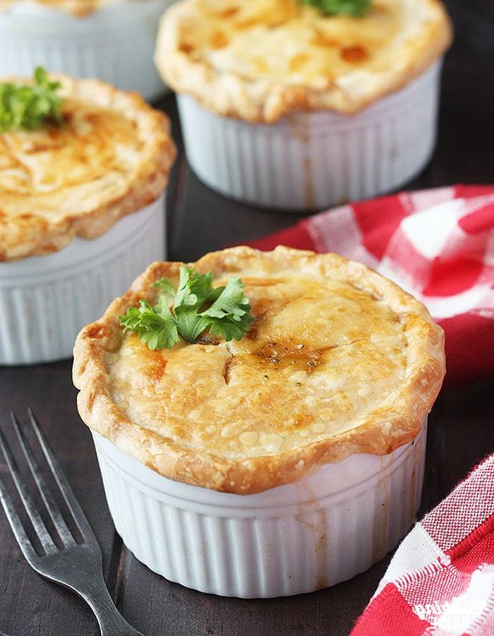 three baked crawfish pies on a wooden background with a red plaid napkin