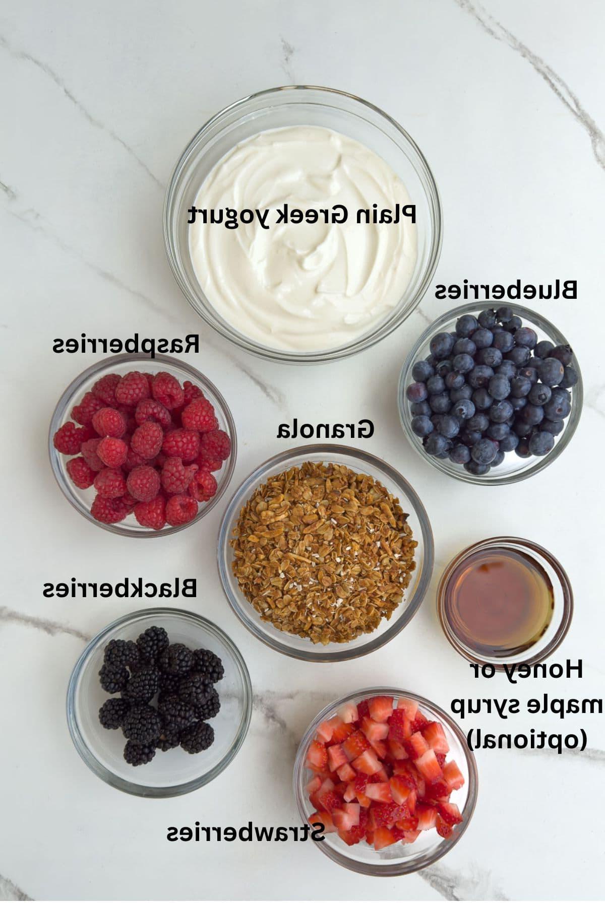 Ingredients for yogurt parfaits in glass bowls on the counter.