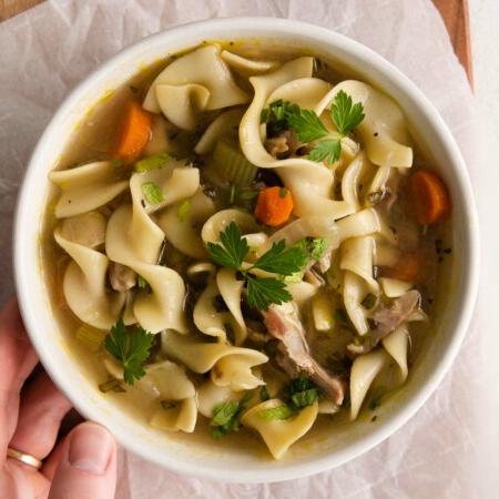 top view image of a bowl of hearty Instant Pot Turkey Soup loaded with veggies, noodles, and carrots with a pop of flavor from garlic and sage.
